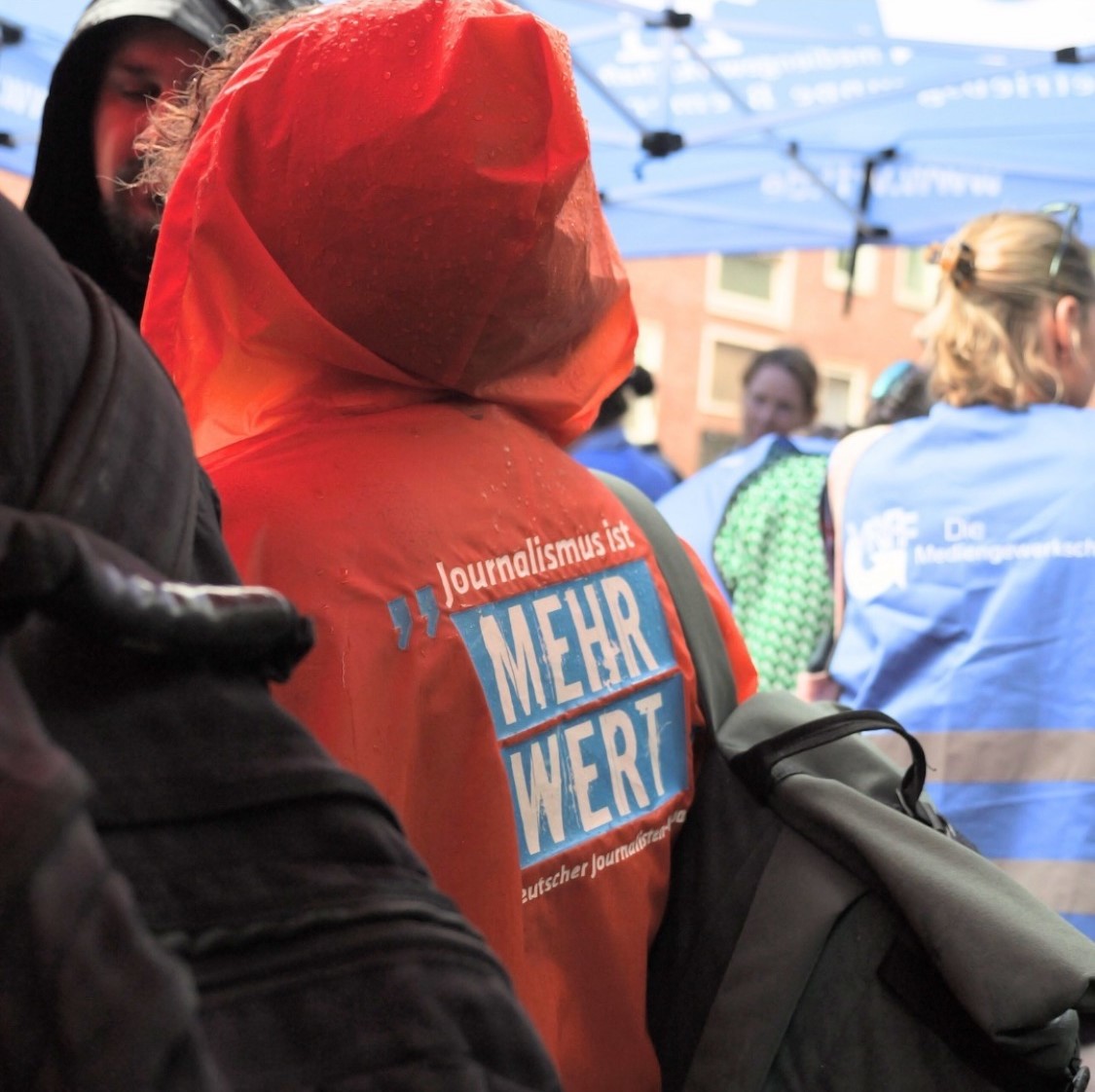 Eine Person trägt eine Regenjacke mit der Aufschrift "Journalismus ist mehr wert". – 